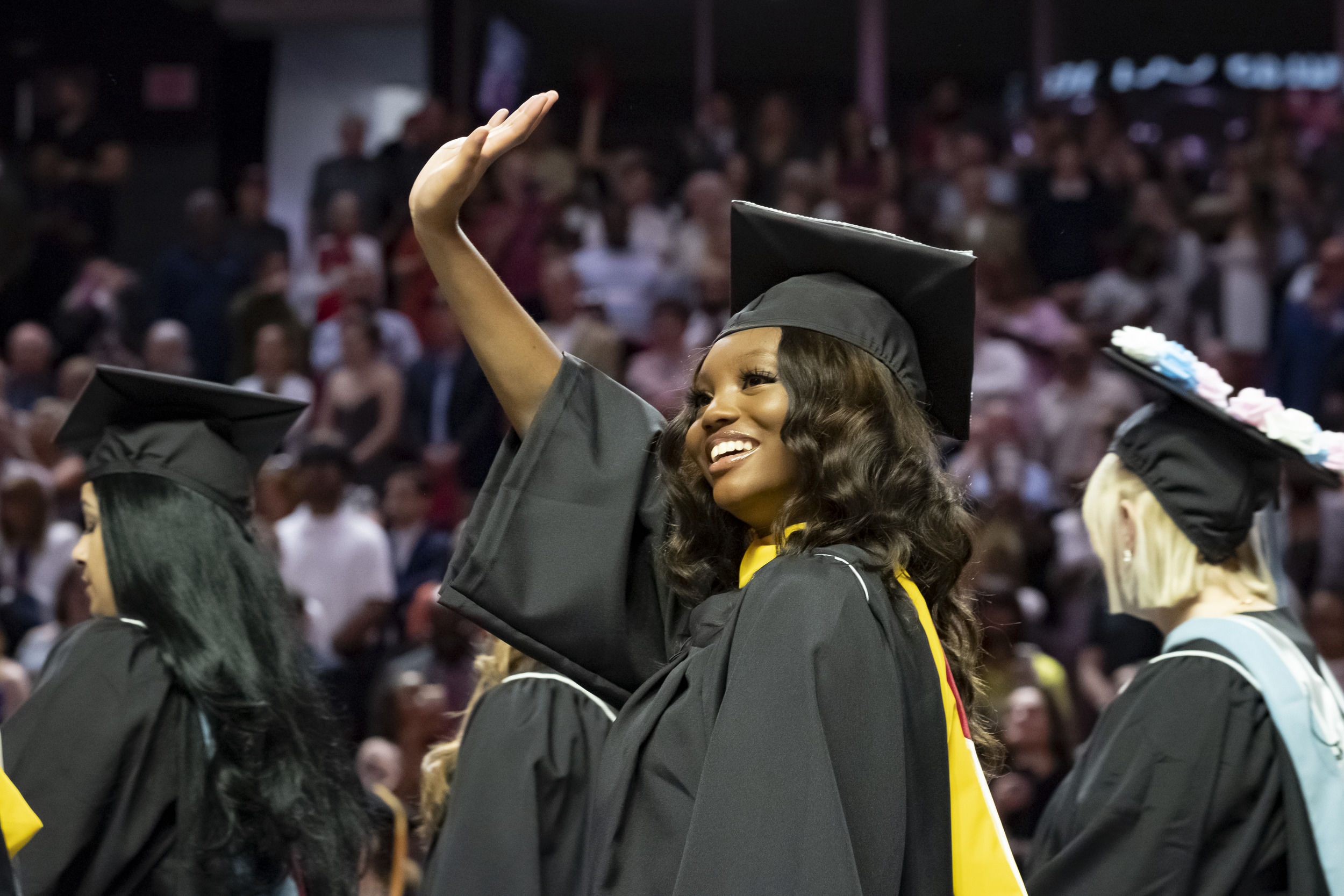 Graduate in cap and gown smiles and waves to spectators