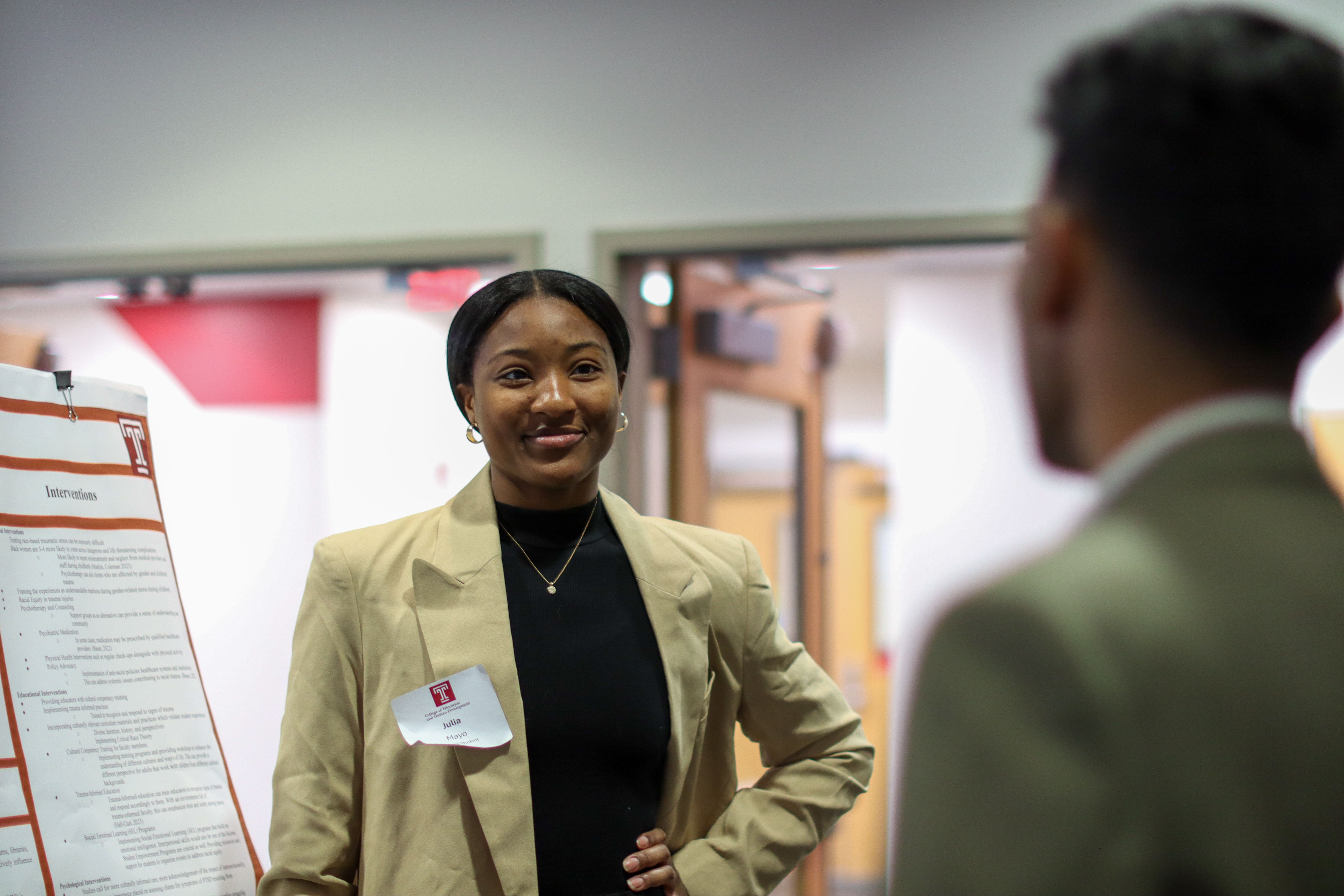 Female student in business attire talks with another student in front of presentation posters