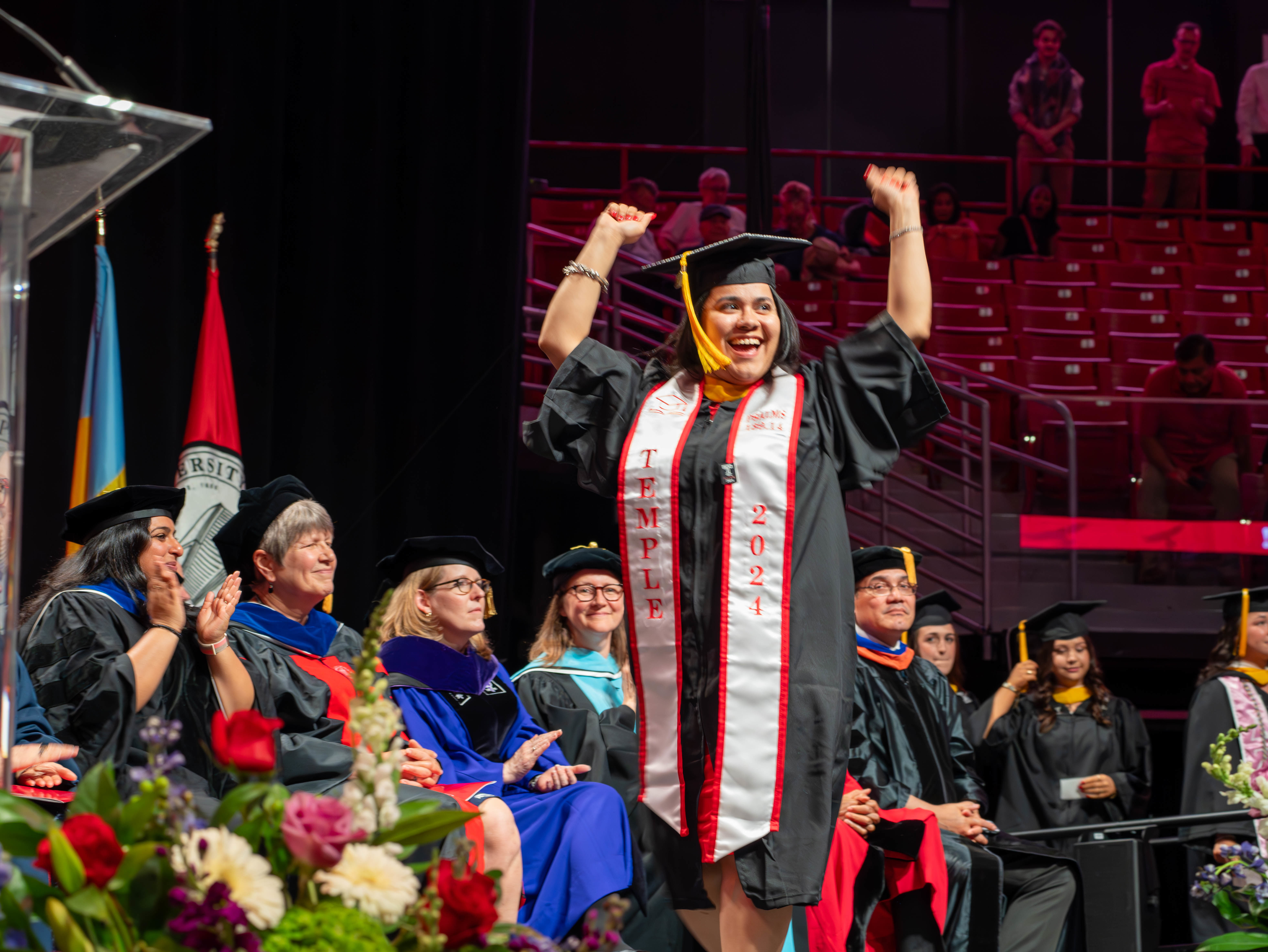 Graduate crossing the stage with arms upraised in celebration