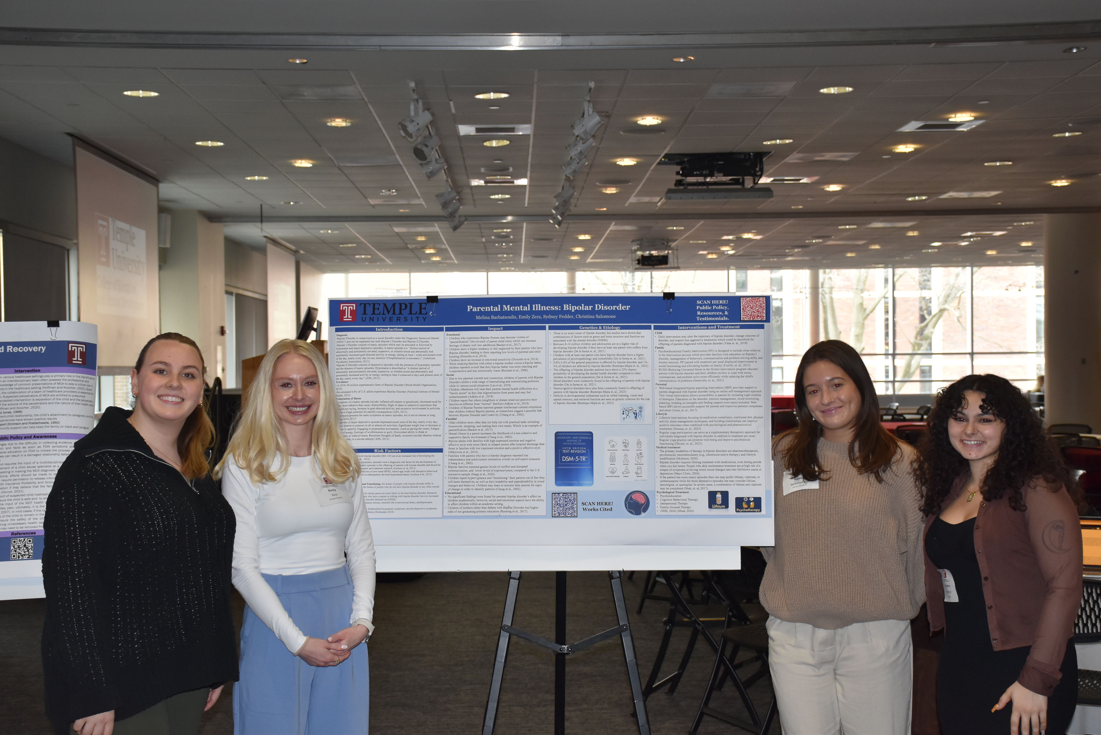 Group of four students pose with large poster display