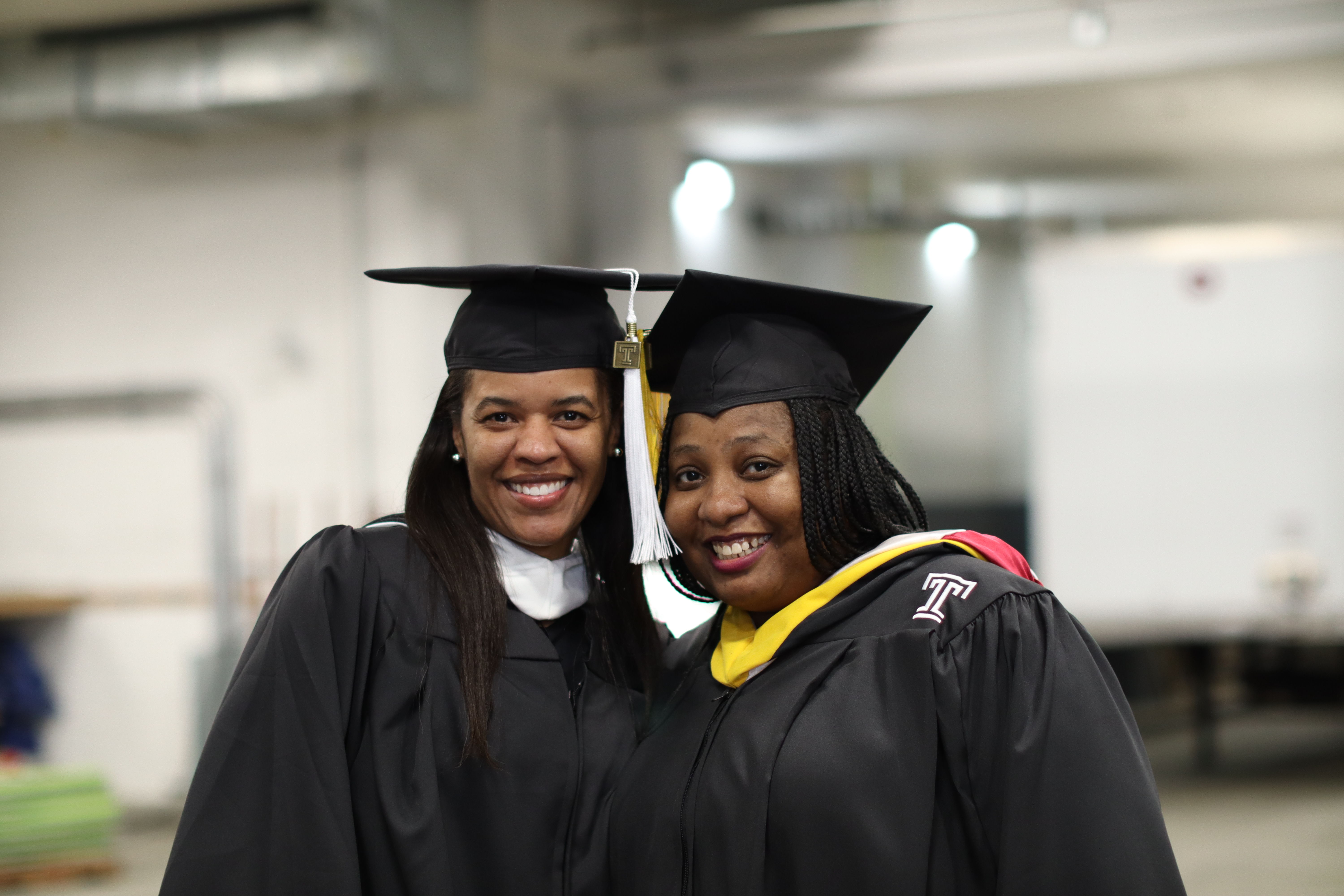 Two students smiling together in their academic regalia before graduation