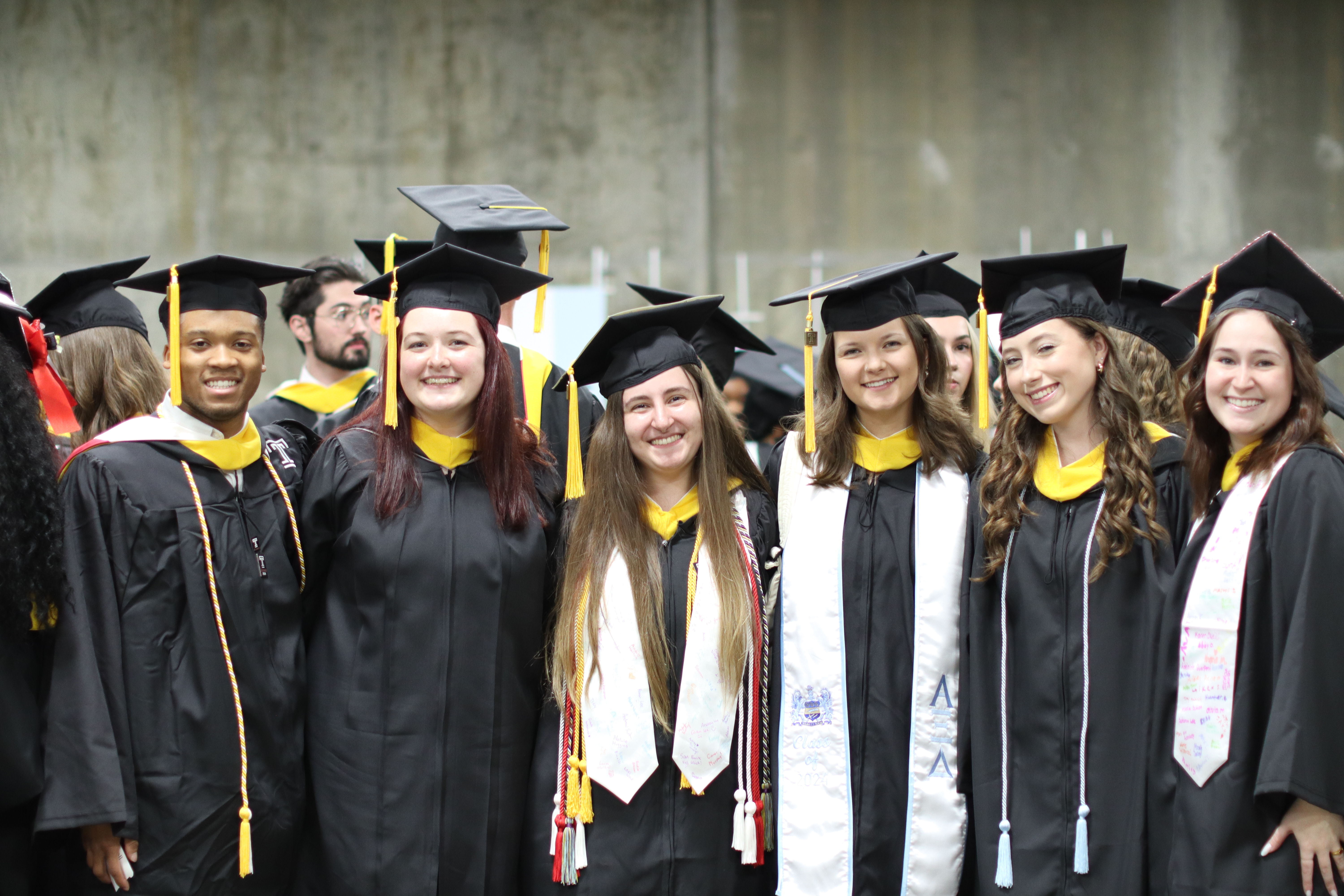 A group of students smiling together in their academic regalia before graduation