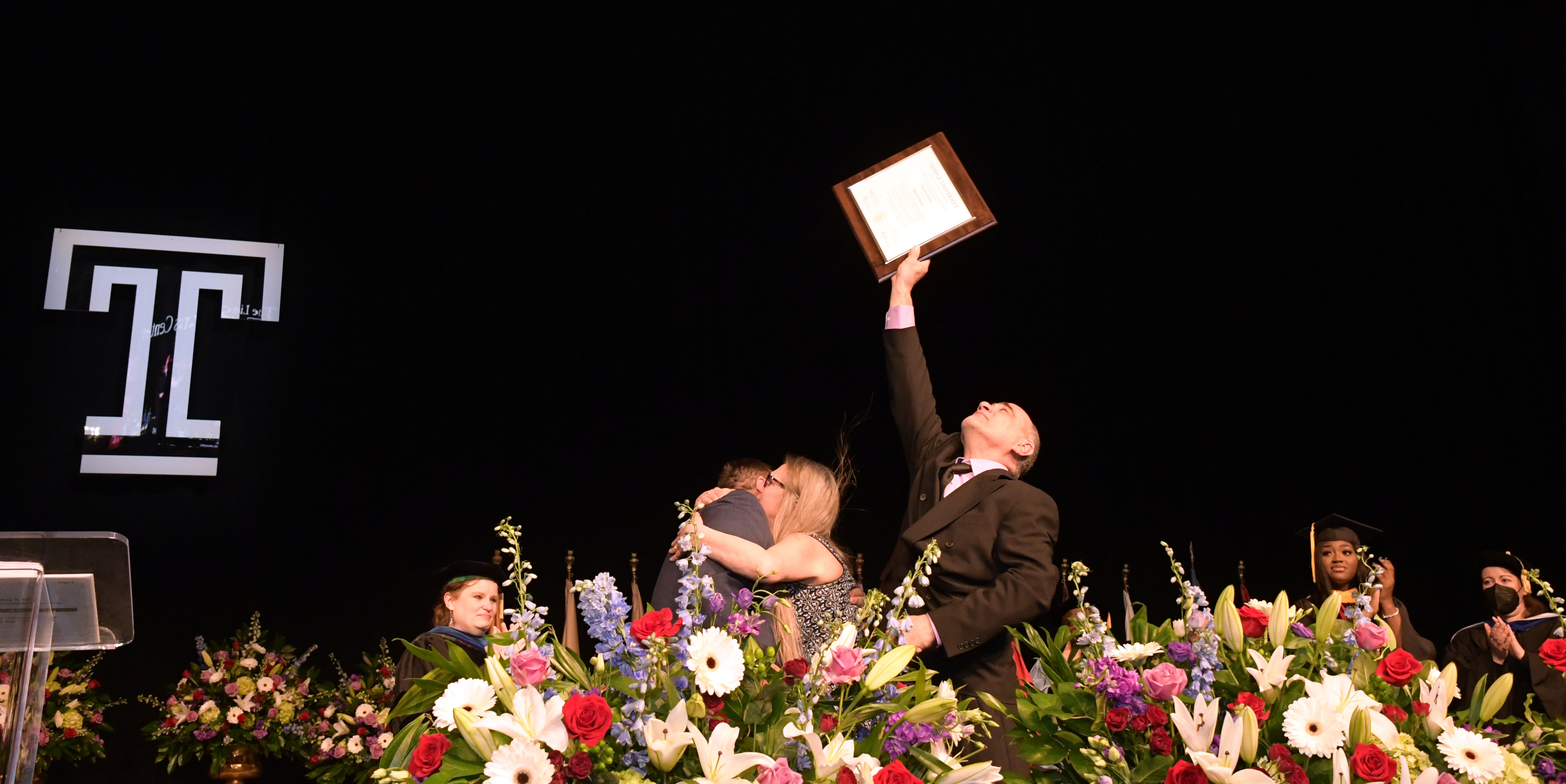 man holds plaque toward the sky while others embrace on the stage