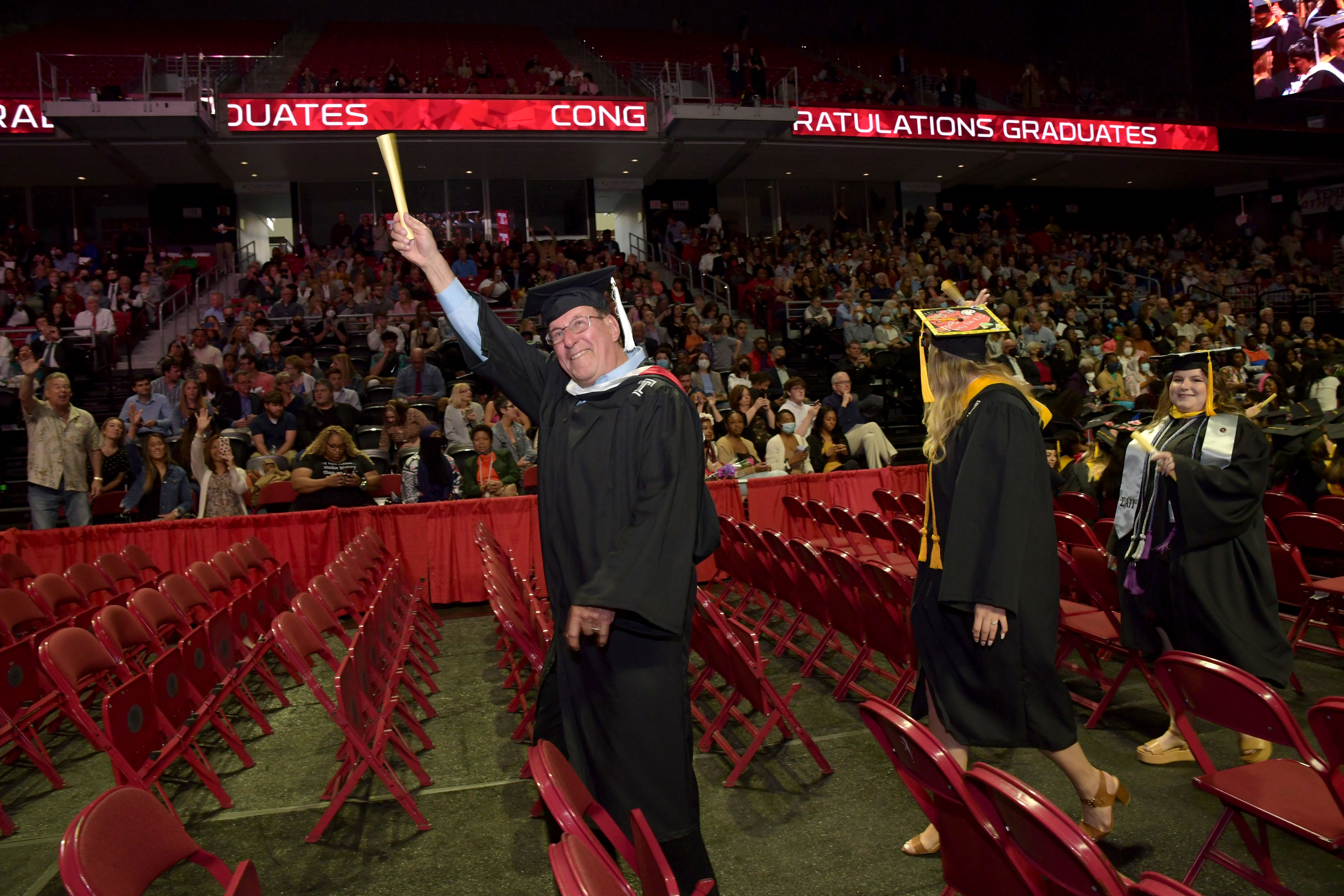 graduate poses with arm raised up holding diploma scroll