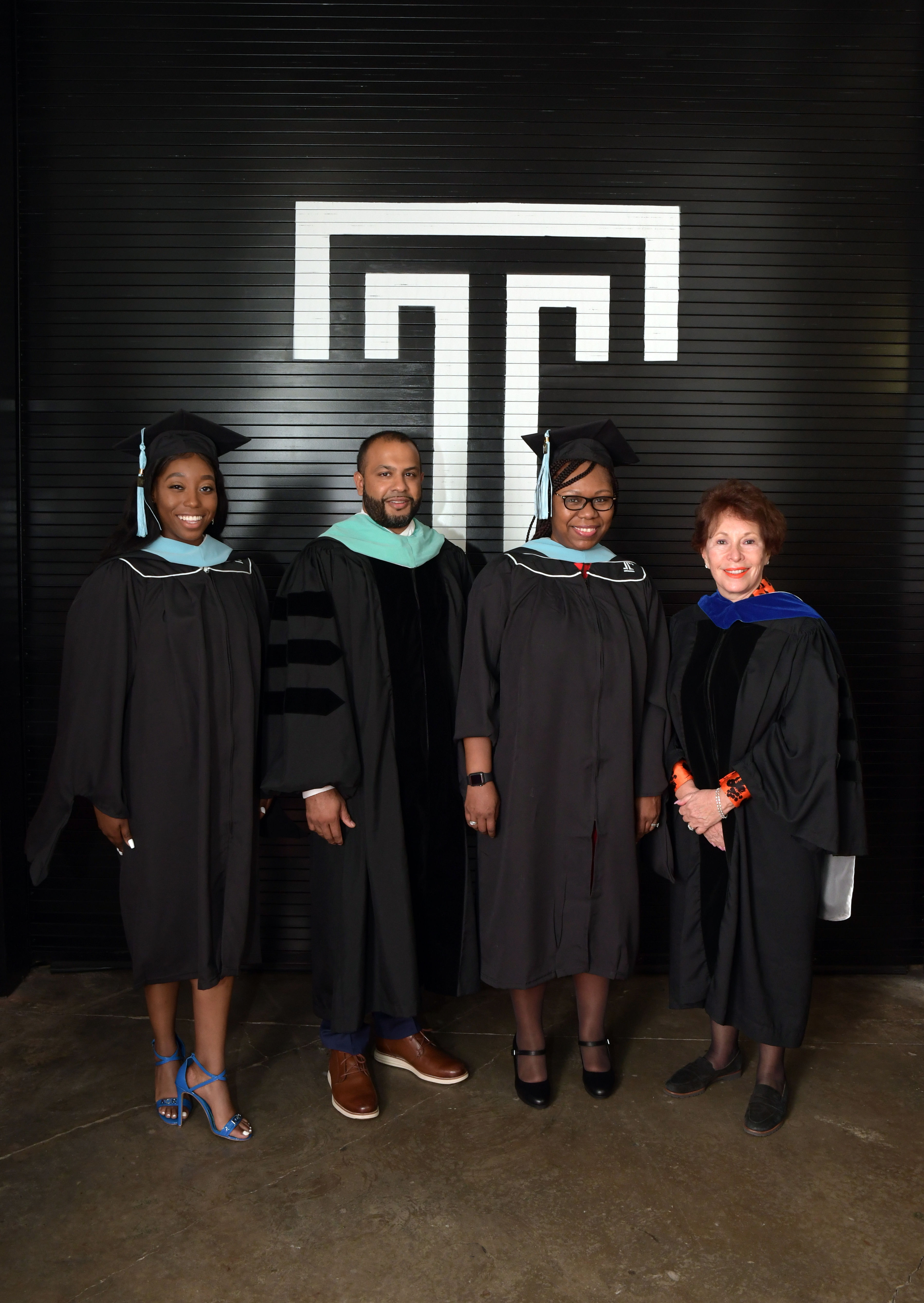four graduation speakers posing in front of black wall with white Temple T