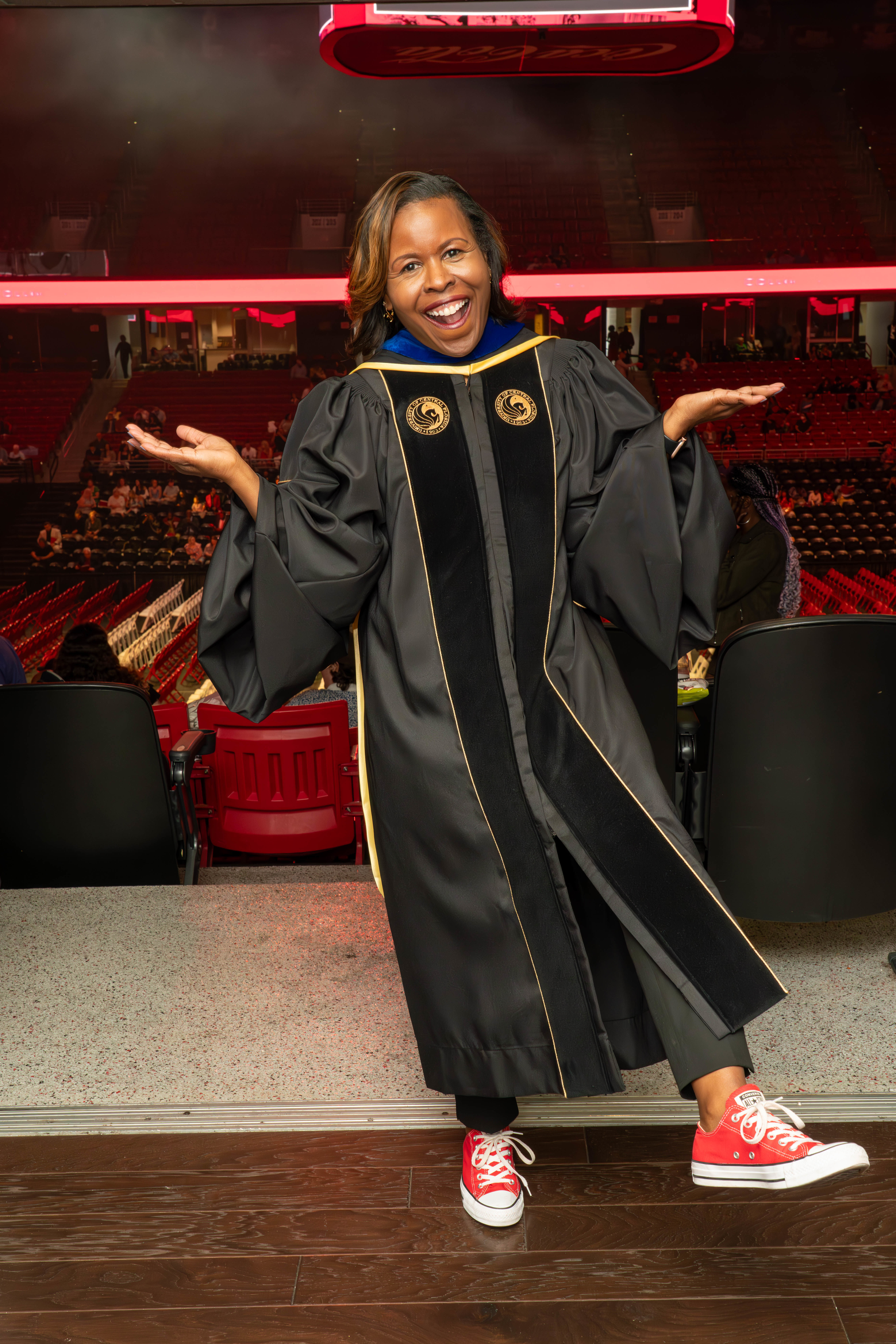 Dean Shealey poses on stage during graduation in her gown and cherry red sneakers