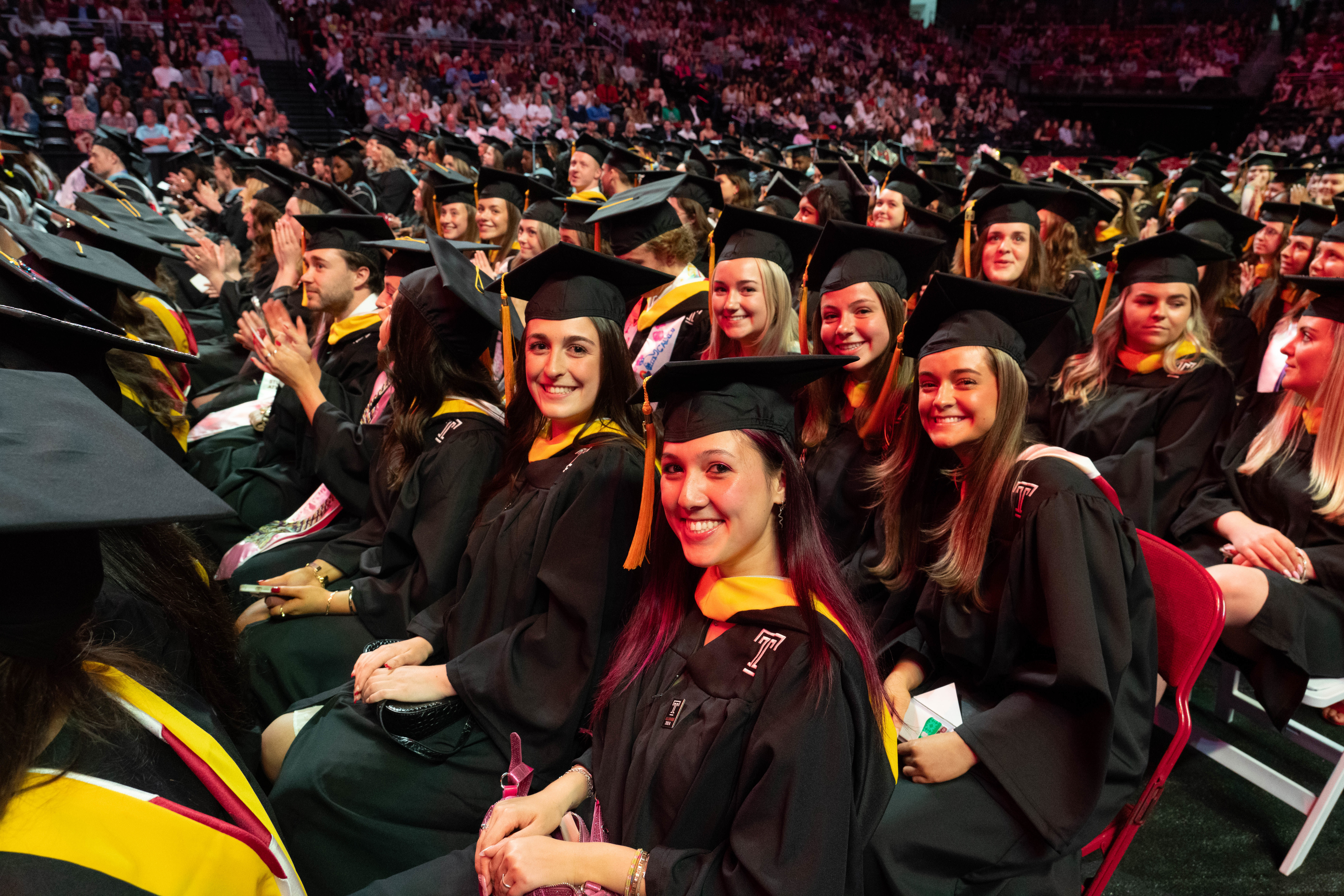 Graduates seated during graduation ceremony, smiling for camera
