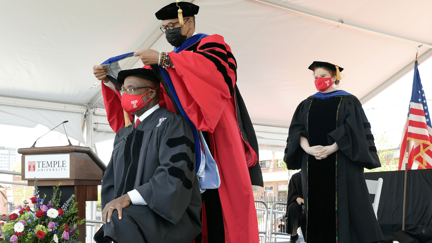 Doctoral graduate kneeling to be hooded by professor on stage