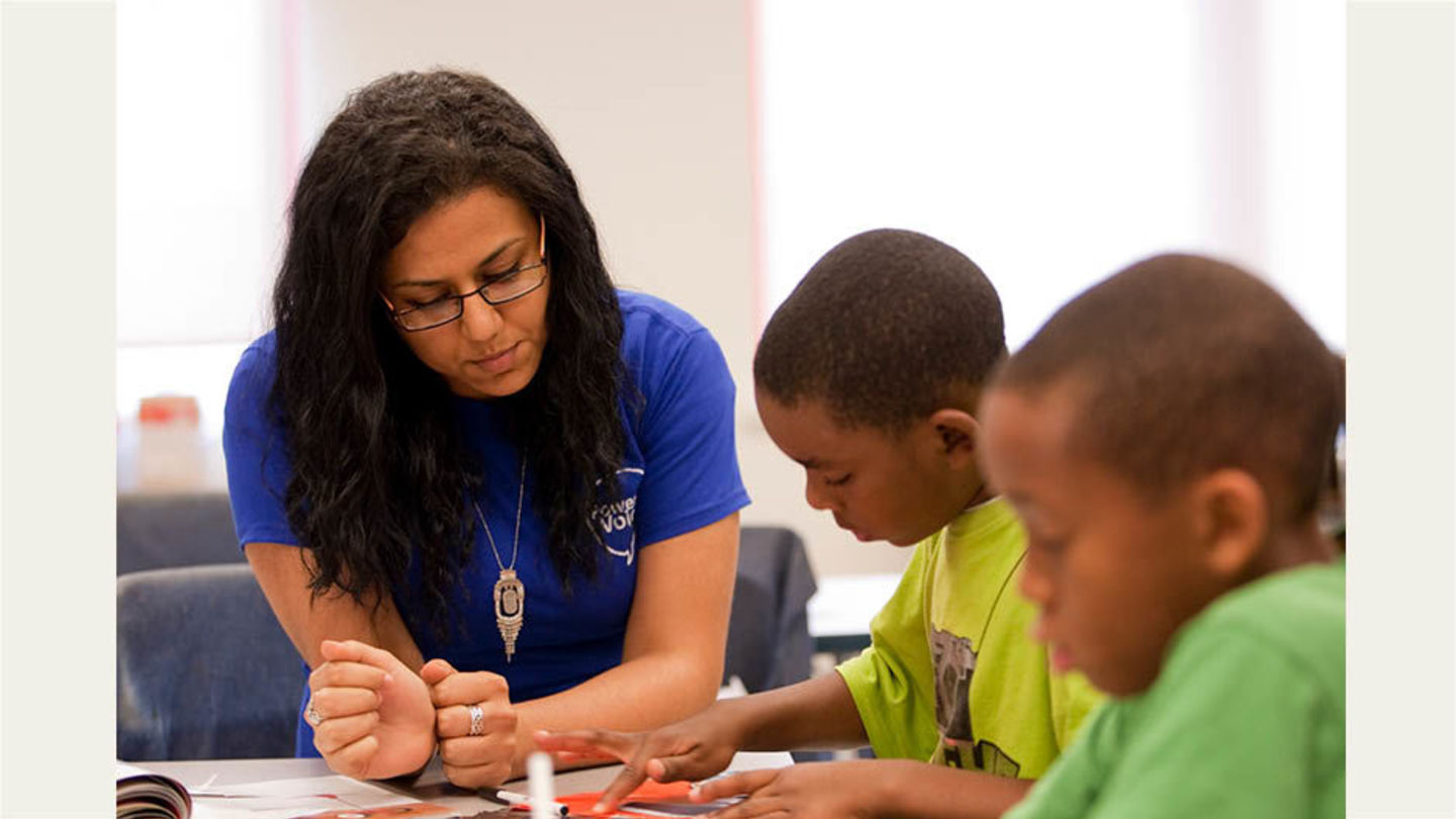 Woman sits at work station engaging with two young children on an art project