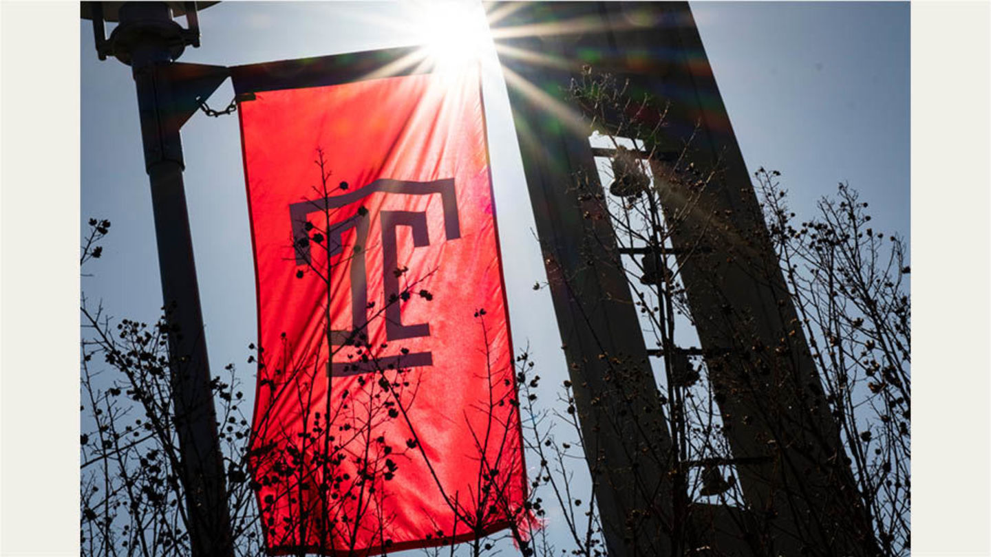 Temple T lightpole flag backlit by the sun, wiht the bell tower in the background