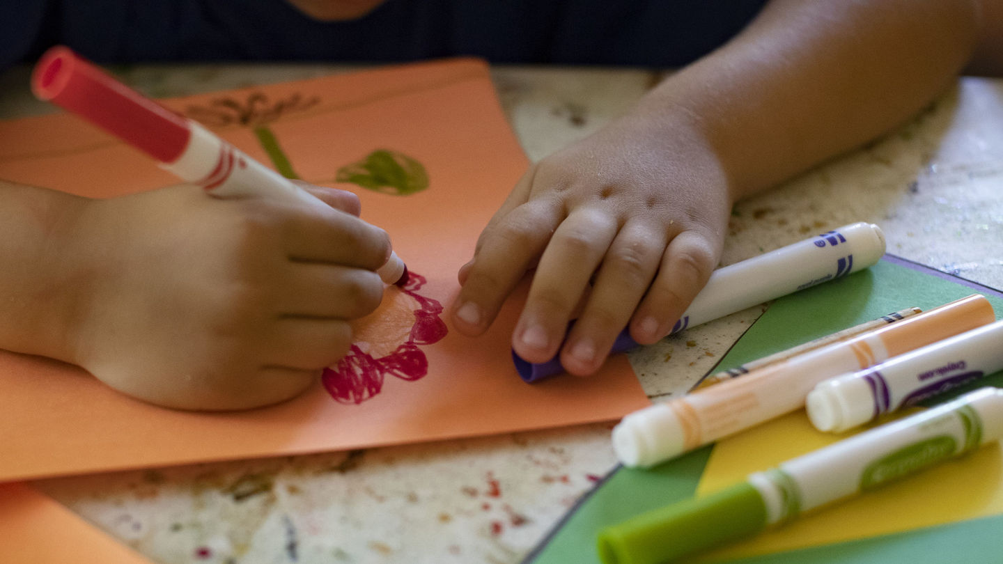 Picture shows hands of student drawing with colorful markers. The picture is used to illustrate for an article on trauma-informed schools.