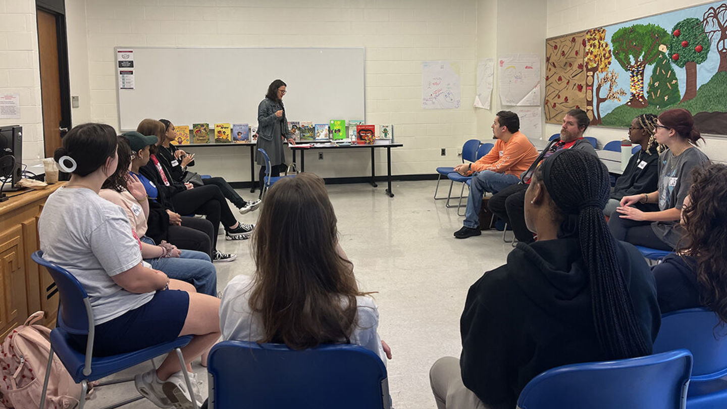 Diverse group of students sits in a semi-circle as an instructor talks to them at the front of the classroom