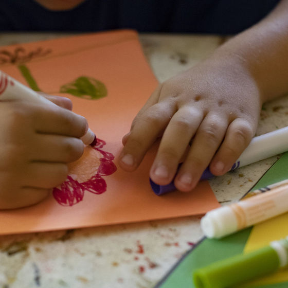 Picture shows hands of student drawing with colorful markers. The picture is used to illustrate for an article on trauma-informed schools.