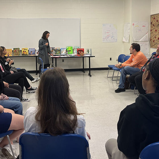 Diverse group of students sits in a semi-circle as an instructor talks to them at the front of the classroom
