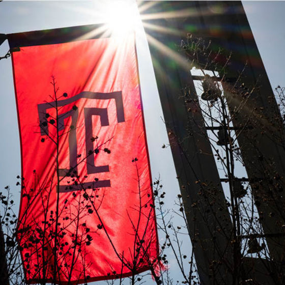 Temple T lightpole flag backlit by the sun, wiht the bell tower in the background