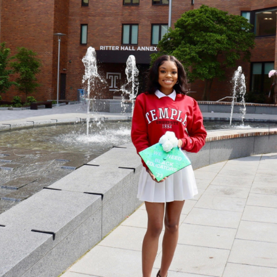 Sydney Smith smiling in her red Temple University sweatshirt in front of Ritter Hall. 