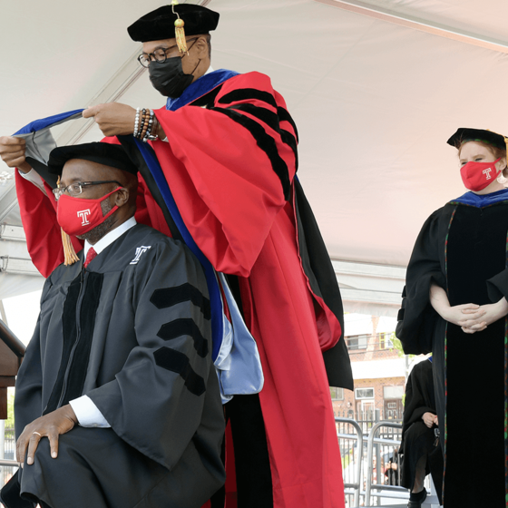Doctoral graduate kneeling to be hooded by professor on stage
